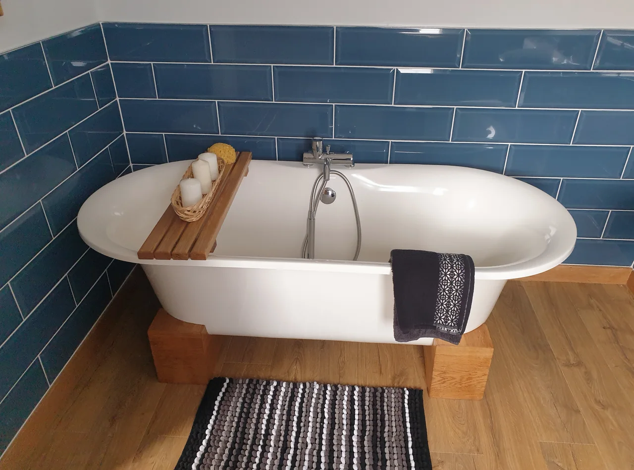A white roll-top bath raised on an oak plinth against blue metro tiling