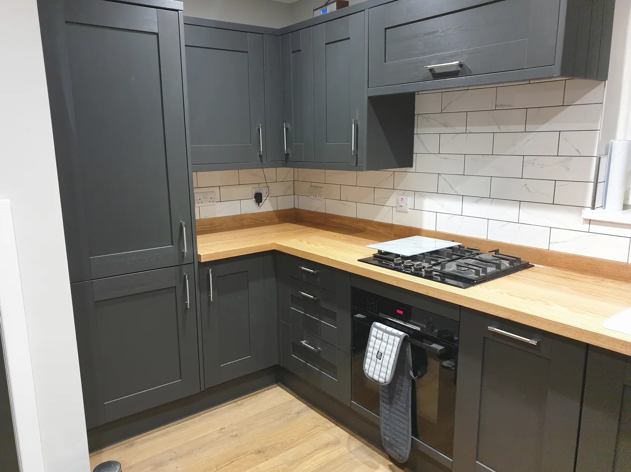 A kitchen with charcoal shaker-style units, a solid oak worktop and marble-effect metro tiling