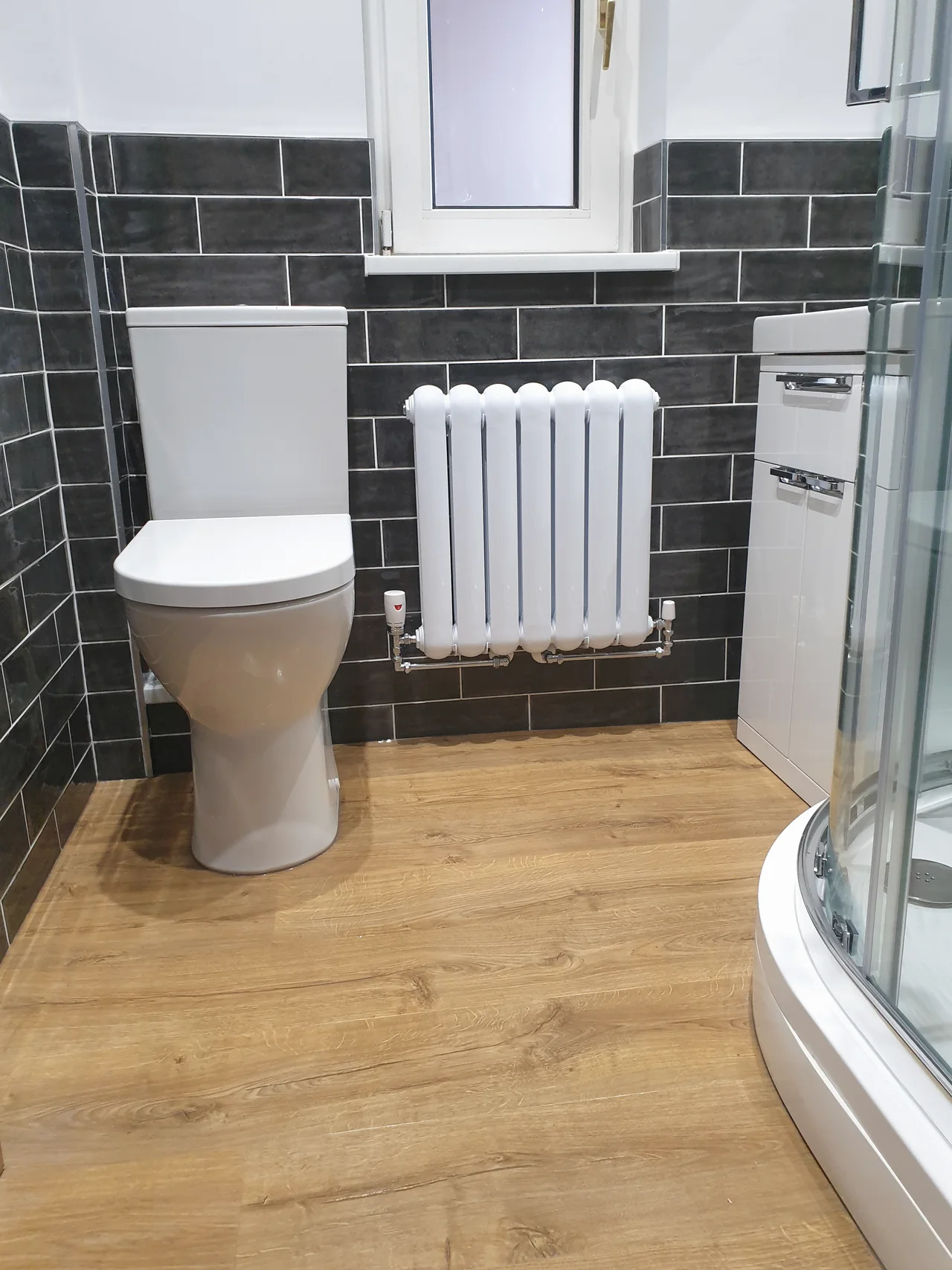 A shower room with dark slate-effect tiling, a quadrant shower enclosure and a white column radiator