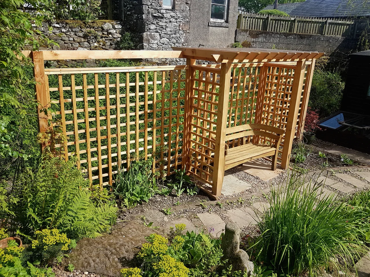 A timber arbour seat built into a lattice trellis screen in a planted garden
