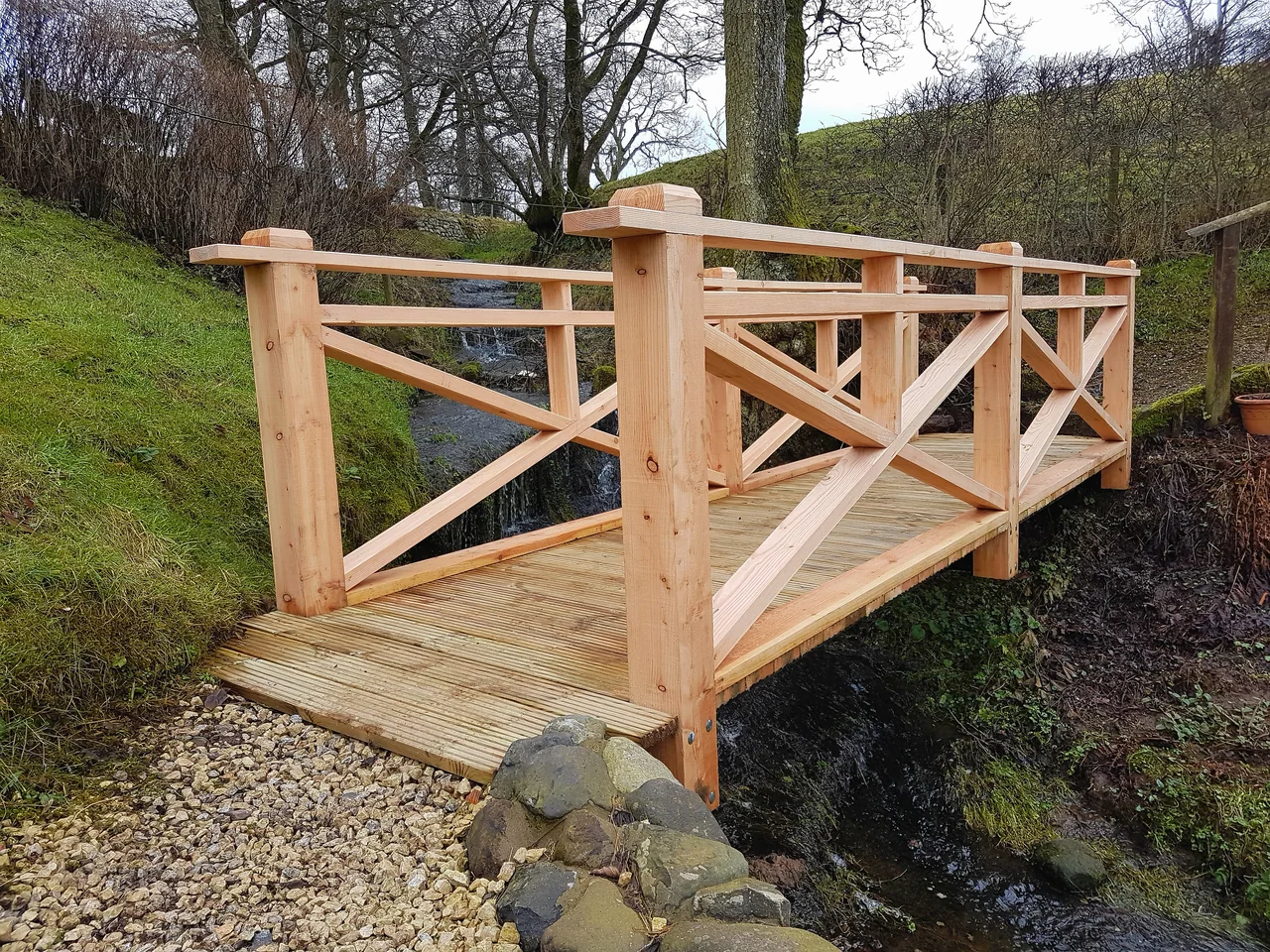 A new timber footbridge with cross-braced handrails spanning a beck in open countryside