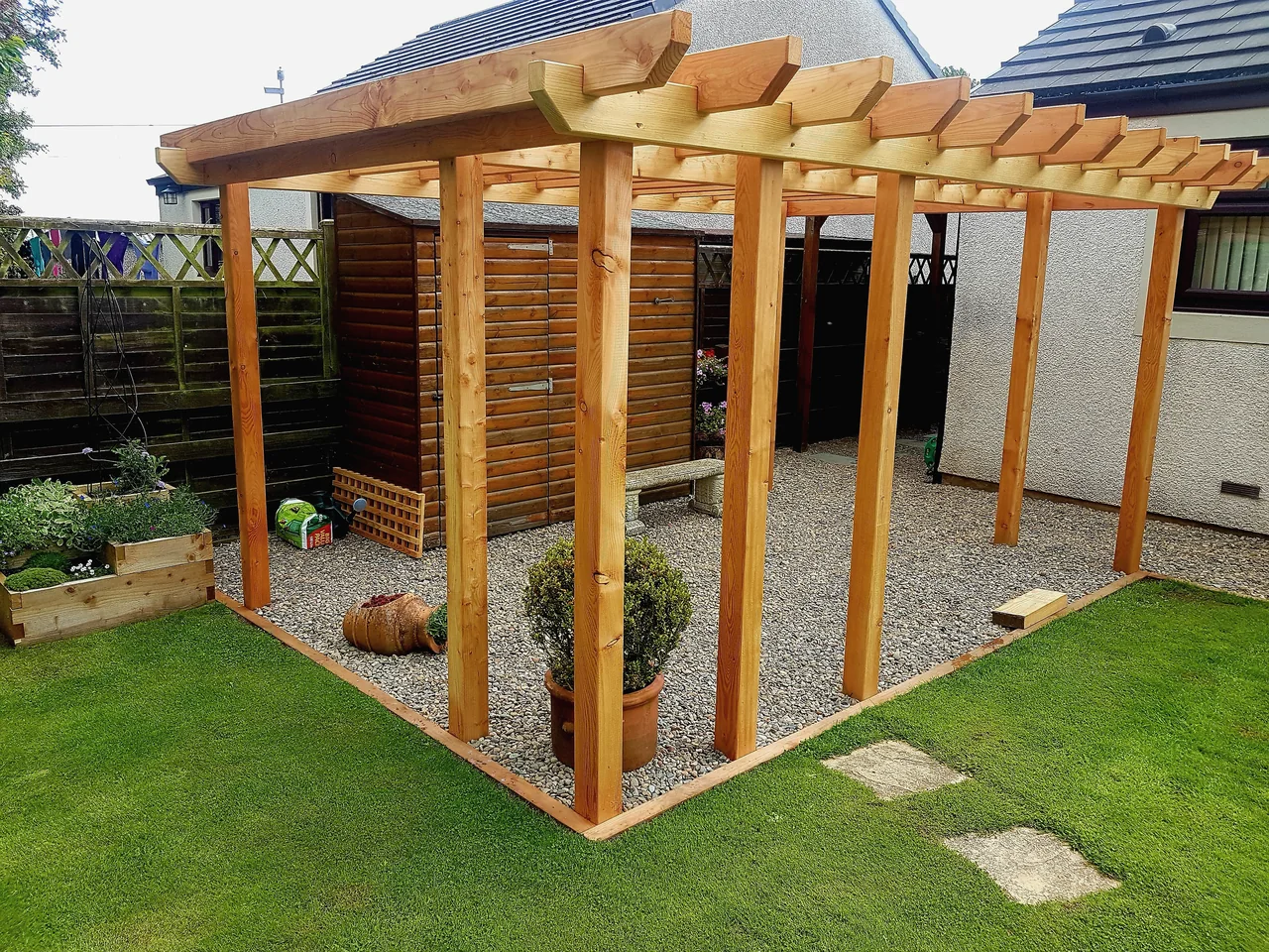 A large freestanding timber pergola with shaped rafter ends standing on a gravel base