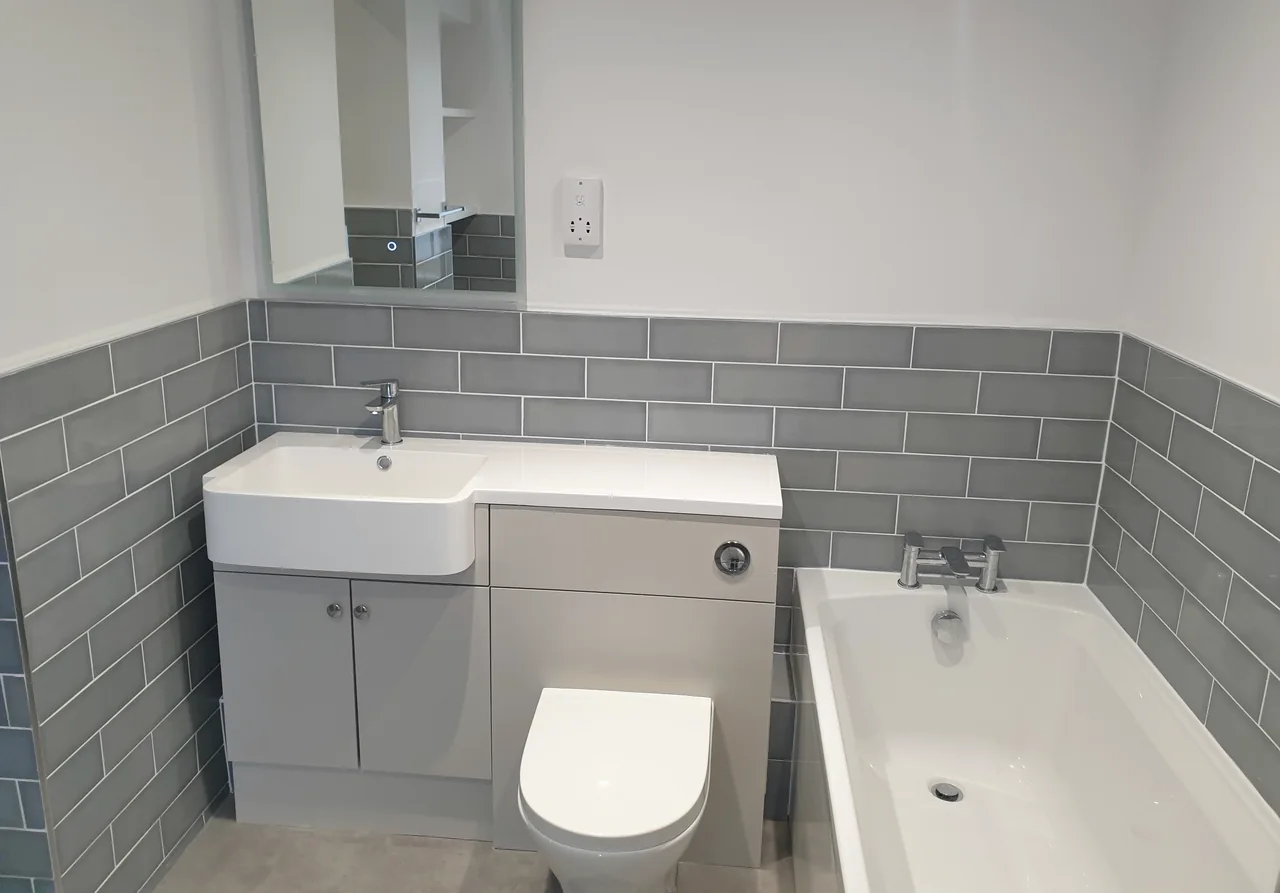 A bathroom with a fitted vanity unit, concealed-cistern toilet and grey metro tiling beside a bath