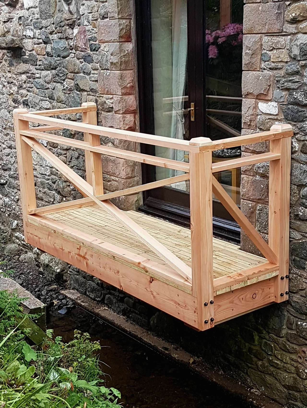 A cantilevered timber platform with braced railings projecting from a stone wall over a beck