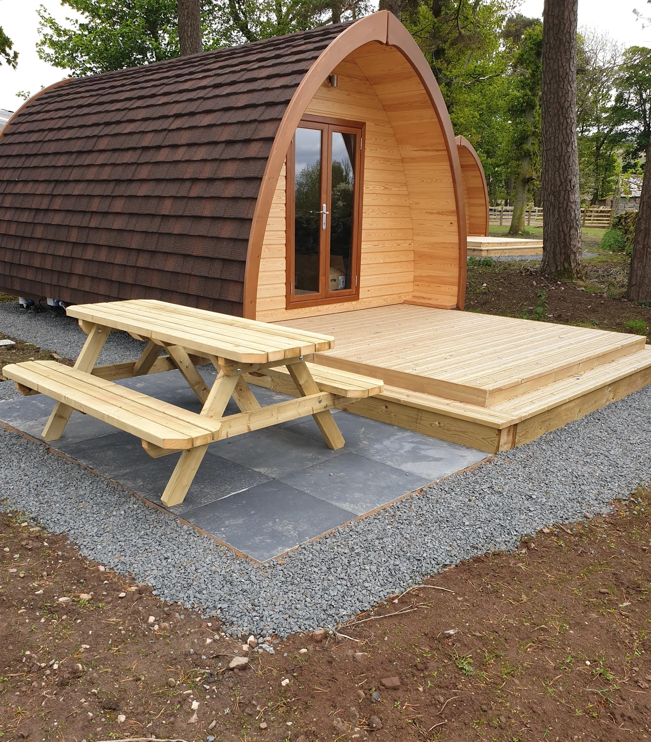 A new timber deck and picnic table laid in front of a shingle-roofed glamping pod