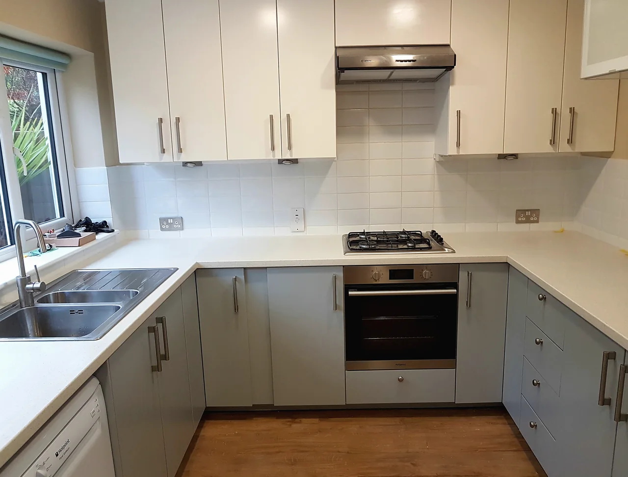 A fitted kitchen with cream wall units above sage green base units and a white worktop